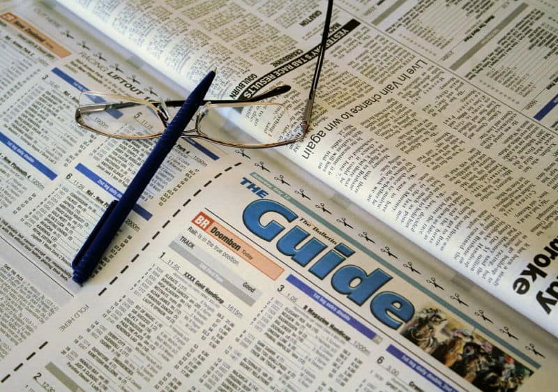 racing pages of newspaper with glasses and pen studying racing form tips